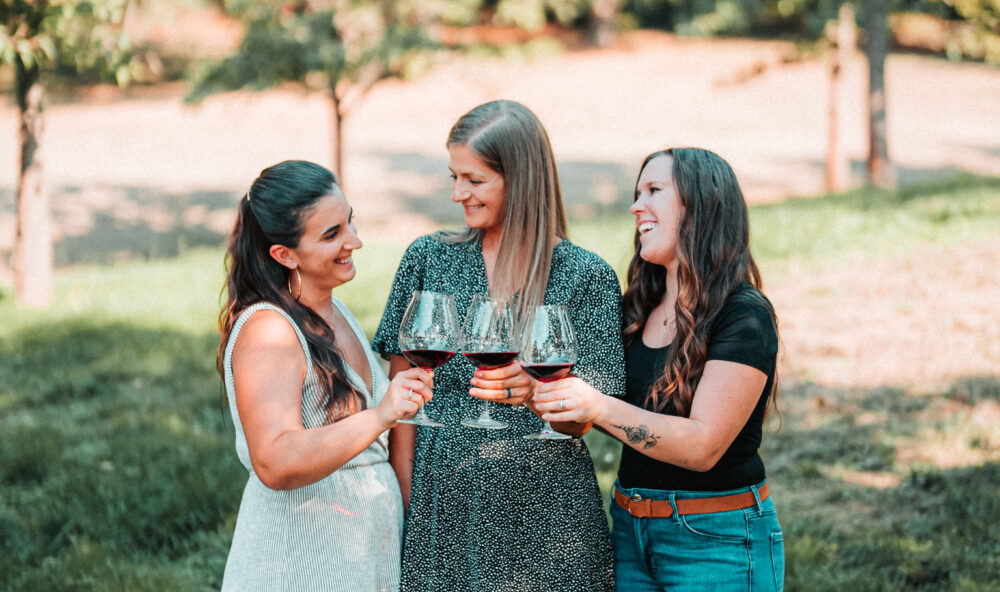 Three women standing outside each holding a glass of wine
